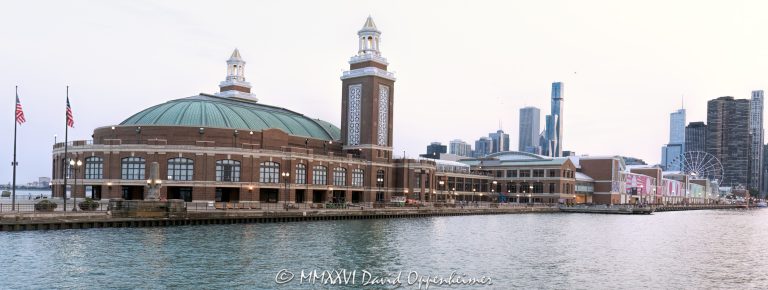 The Aon Grand Ballroom at Navy Pier, part of the pier’s original 1916 construction, fills the foreground in a Lake Michigan view toward the Chicago skyline. Its green domed roof and lantern-topped towers rise behind two flags, while the Terminal Building, Offshore Rooftop and Centennial Wheel recede along the diagonal pier beneath a pale sky in Chicago, Illinois – © 2026 David Oppenheimer – Performance Impressions photography archives https://performanceimpressions.com Navy Pier Auditorium, Aon Grand Ballroom, 600 East Grand Avenue, Navy Pier Chicago, Navy Pier Terminal Building, Navy Pier Shelter Building, Offshore Rooftop, Offshore Rooftop and Bar, Centennial Wheel, Navy Pier, auditorium exterior, ballroom exterior, building exterior, facade, architecture, Chicago Landmark, green domed roof, domed roof, twin towers, concert hall towers, lantern towers, brick facade, terra cotta, two flags, flags, flagpoles, East End Plaza, North Dock, North Dock Road, East Grand Avenue, Lake Michigan, Chicago Harbor, Chicago waterfront, Chicago lakefront, Chicago skyline, Chicago cityscape, skyline, city skyline, cityscape, skyline view, waterfront skyline, lakefront skyline, urban skyline, city view, lake view, postcard view, Chicago postcard, Navy Pier postcard, pale sky, Visit Chicago, Visit Navy Pier, Chicago tourism, Chicago travel, Chicago attractions, Chicago landmarks, things to do in Chicago, tourist attraction, travel destination, sightseeing, tourism, travel, shopping, Navy Pier shopping, dining, Navy Pier dining, Navy Pier restaurants, entertainment, Ferris wheel, Chicago Ferris wheel, observation wheel, Navy Pier Salute, World War II memorial, Bob Newhart Statue, Grand Ballroom, Municipal Pier, Municipal Pier No. 2, Charles Sumner Frost, Frost and Granger, Arts and Crafts architecture, Edward C. Shankland, William Artingstall, KOO, Maverick Hospitality, Dutch Wheels, Aon plc, Streeterville, Chicago, Illinois, Cook County, Great Lakes, USA, United States, 60611, travel photography, tourism photography, postcard photography, cityscape photography, destination imagery, landmark photography, Licensing, image licensing, commercial imagery, photography licensing, art, print, fine art, commercial photography, David Oppenheimer, horizontal, 1-15213827141