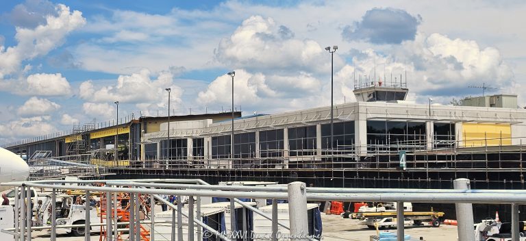Asheville Regional Airport AVL Forward terminal construction in Fletcher near Asheville, North Carolina, viewed from the airport apron with scaffolding and exposed structural steel framing revealing the open terminal structure during construction. The airport terminal modernization and expansion was designed by Gresham Smith and is being built by Hensel Phelps for the Greater Asheville Regional Airport Authority – © 2026 David Oppenheimer – Performance Impressions photography archives https://performanceimpressions.com Asheville Regional Airport, Asheville Airport, Asheville Regional, Asheville airport terminal, Asheville terminal, Asheville airport construction, Asheville construction, Asheville airport expansion, AVL Forward, AVL Forward terminal, AVL Forward project, AVL terminal, AVL terminal construction, AVL construction, AVL airport, AVL, KAVL, airport terminal, terminal, terminal construction, airport construction, terminal expansion, airport expansion, terminal modernization, airport modernization, terminal renovation, new terminal, new airport terminal, airport building, terminal building, building construction, construction, construction site, construction project, construction progress, under construction, building under construction, unfinished building, unfinished structure, work in progress, scaffolding, scaffold, scaffolds, structural steel, steel structure, steel frame, steel framing, exposed steel, exposed structure, exposed framing, girders, girder, steel girders, beams, beam, steel beams, columns, steel columns, structural frame, building frame, open structure, open framing, building structure, structural construction, steel construction, construction detail, construction architecture, architecture, airport architecture, terminal architecture, aviation architecture, architectural construction, architectural engineering, engineering, structural engineering, civil engineering, infrastructure, airport infrastructure, aviation infrastructure, transportation infrastructure, infrastructure construction, commercial construction, large scale construction, capital project, airport development, airport improvement, terminal development, aviation construction, airside construction, airport operations, construction operations, airport apron, apron, aircraft apron, airport ramp, ramp, tarmac, airfield, airside, airport ground, ground boarding, passenger operations, aviation, airport, regional airport, commercial airport, transportation, air travel, Gresham Smith, Gresham Smith Asheville, Gresham Smith aviation, architect, architects, airport architect, terminal architect, aviation architect, architecture firm, Brad Sucher, structural engineer, civil engineer, engineering firm, interior design, airport planning, terminal planning, experiential design, wayfinding, Hensel Phelps, Hensel Phelps Construction, Hensel Phelps Asheville, construction manager, construction management, CM at Risk, contractor, general contractor, airport contractor, aviation contractor, Greater Asheville Regional Airport Authority, Asheville Regional Airport Authority, GARAA, airport authority, Asheville, Asheville North Carolina, North Carolina, NC, Western North Carolina, WNC, Fletcher, Fletcher North Carolina, Henderson County, Buncombe County, Blue Ridge, Blue Ridge Mountains, 61 Terminal Drive, Terminal Drive, Airport Road, 28732, United States, USA, airport photography, construction photography, architecture photography, architectural photography, infrastructure photography, aviation photography, transportation photography, industrial photography, documentary photography, editorial photography, commercial photography, Asheville photography, North Carolina photography, construction art, architecture art, airport art, Asheville art, photographic print, fine art print, archival print, gallery print, collector print, wall art, licensing, image licensing, commercial imagery, photography licensing, art, print, fine art, commercial photography, clouds, sunny, blue sky, summer, David Oppenheimer, Performance Impressions, Performance Impressions photography archives, horizontal, 1-15156784411