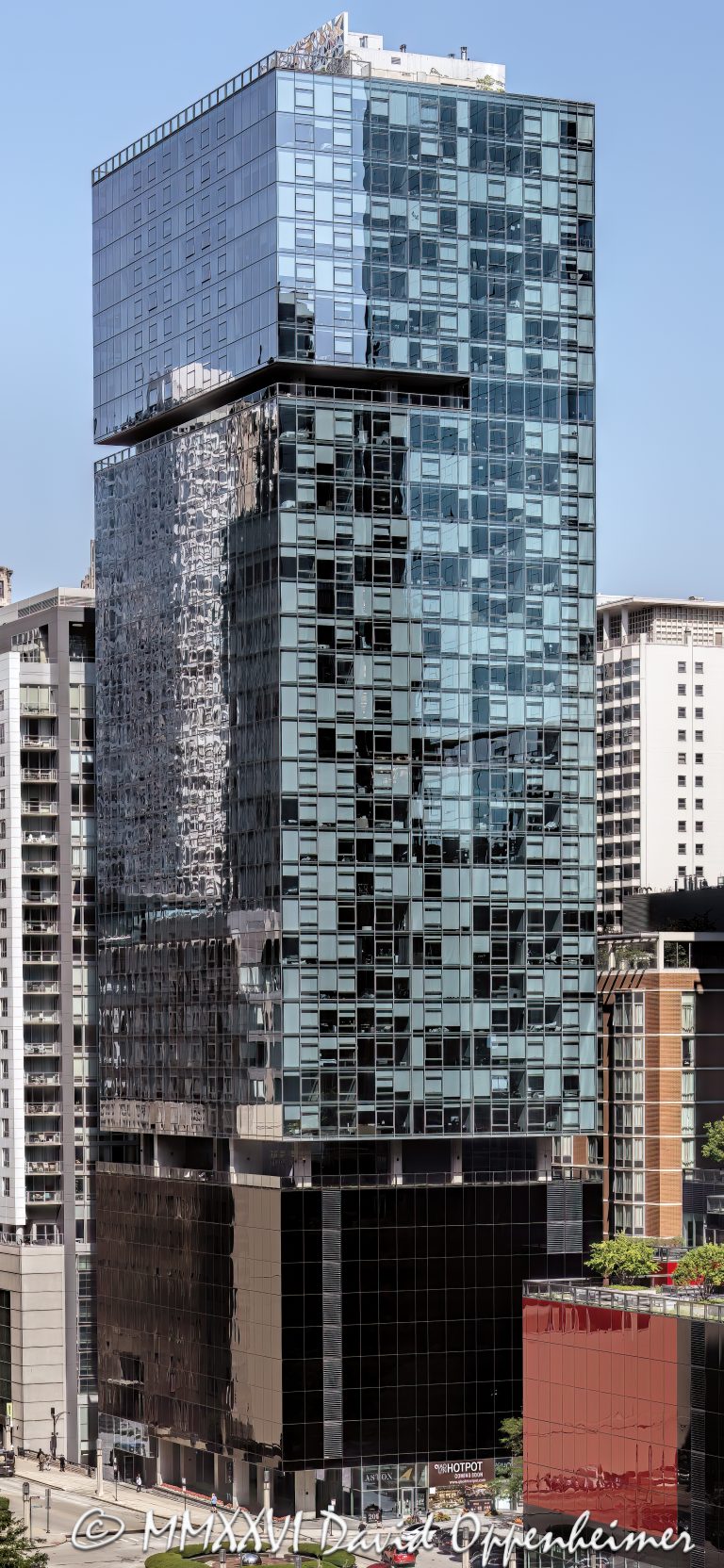 Aston Apartments at 200 East Illinois Street in Chicago, Illinois, located in the Streeterville neighborhood near Michigan Avenue, the Chicago Riverwalk, and Lake Michigan. Contemporary residential high-rise architecture designed by David Hovey of Optima, Inc. featuring a glass facade, dark glass podium, balconies, and luxury rental residences. The 42-story apartment building opened in 2013 and was formerly known as Optima Center Chicago – © 2026 David Oppenheimer – Performance Impressions photography archives https://performanceimpressions.com Aston Apartments, Aston Chicago, Aston Chicago Apartments, Aston Luxury Apartments, Aston, Optima Center, Optima Center Chicago, 200 East Illinois, 200 East Illinois Street, 200 E Illinois, East Illinois Street, Illinois Street, Chicago, Chicago Illinois, Illinois, United States, 60611, Streeterville, Downtown Chicago, Chicago Loop, Magnificent Mile, Michigan Avenue, Chicago Riverwalk, Lake Michigan, architecture, Chicago architecture, architectural photography, facade, building exterior, exterior, residential architecture, modern architecture, contemporary architecture, urban architecture, apartment tower, apartment building, rental apartments, luxury apartments, residential tower, residential building, high-rise, skyscraper, building, tower, glass tower, glass building, glass facade, dark glass, dark glass podium, curtain wall, balconies, balcony, podium, residential real estate, apartment real estate, Chicago real estate, real estate, downtown apartments, Streeterville apartments, Chicago apartments, luxury rentals, urban living, city living, mixed-use building, retail space, commercial architecture, downtown, urban, iconic building, American architecture, Illinois architecture, daylight, multifamily housing, Optima Inc, David Hovey, DeBartolo Development, Greystar, commercial photography, commercial imagery, image licensing, licensing, photography licensing, David Oppenheimer, vertical, 1-15156784411