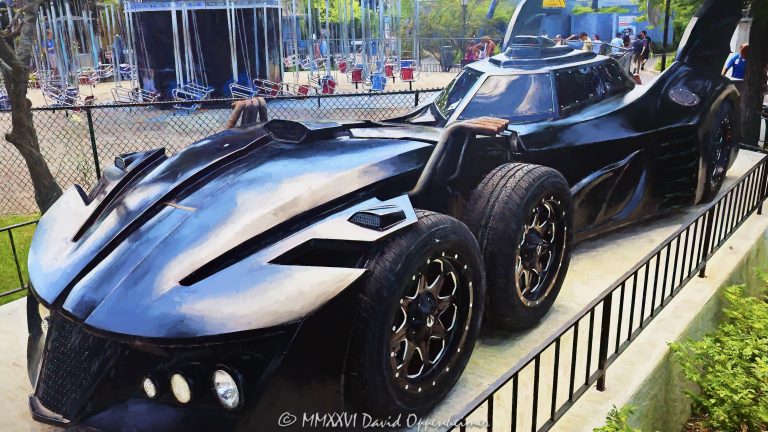 Six-wheel Batmobile at Six Flags Great America near Chicago in Gurnee, Illinois, shown in close-up in the amusement park’s DC Universe themed area. The futuristic black Batman vehicle features a multi-axle design with four closely spaced front wheels, an aircraft-style cockpit canopy, tall vertical batwing fins and multiple exposed exhaust pipes, creating a distinctive comic-book-inspired interpretation of Batman’s iconic car – © 2026 David Oppenheimer – Performance Impressions photography archives https://performanceimpressions.com Batmobile, Six Flags Batmobile, Six Flags Great America Batmobile, Great America Batmobile, Batman Batmobile, Batmobile Chicago, Chicago Batmobile, Batmobile Illinois, six-wheel Batmobile, six-wheeled Batmobile, six wheels, six-wheel vehicle, six-wheeled vehicle, multi-axle, multi-axle vehicle, dual front axle, twin front axle, front axles, four front wheels, Batman car, Batman vehicle, Batmobile car, Batmobile vehicle, Batmobile display, Batman display, vehicle display, display vehicle, show car, superhero car, superhero vehicle, futuristic Batmobile, futuristic car, futuristic vehicle, custom car, custom vehicle, black Batmobile, black car, black vehicle, automobile, automotive, car, vehicle, transportation, automotive design, vehicle design, futuristic design, aerodynamic, aerodynamic design, bodywork, sculpted bodywork, vehicle exterior, car exterior, exterior, close up, close-up, detail, vehicle detail, automotive detail, wheels, wheel, tires, tire, wheel design, front wheels, cockpit, cockpit canopy, aircraft-style cockpit, aircraft cockpit, canopy, enclosed cockpit, windshield, windscreen, batwing fins, bat wings, rear fins, vertical fins, tail fins, Batman fins, exhaust, exhaust pipes, eight exhaust pipes, multiple exhausts, side exhaust, exhaust detail, pipes, side intakes, air intakes, vents, Batman, BATMAN, Batman DC, DC Batman, DC Comics, DC Comics Batman, DC, DC Universe, Six Flags DC Universe, DC Universe Six Flags, Great America DC Universe, DC Universe Chicago, DC Universe Illinois, superhero, superheroes, DC superhero, comic book, comics, comic books, comic character, comic superhero, superhero icon, Batman icon, Batman memorabilia, DC memorabilia, Batman attraction, Batman theme, Batman themed, Batman experience, themed vehicle, themed entertainment, comic-book inspired, comic inspired, fantasy vehicle, fictional vehicle, entertainment vehicle, photo op, Six Flags Great America, Six Flags Great America Chicago, Great America Chicago, Great America Illinois, Six Flags Chicago, Six Flags Illinois, Six Flags, Great America, amusement park, theme park, amusement parks, theme parks, amusement park attraction, theme park attraction, park attraction, attraction, attractions, entertainment, family entertainment, tourist attraction, travel destination, destination, Gurnee, Gurnee Illinois, Gurnee IL, Illinois, Lake County, Lake County Illinois, northern Illinois, Chicagoland, Chicago area, Chicago, Chicago Illinois, Chicago attraction, Chicago attractions, Chicago theme park, Chicago amusement park, Chicago tourism, Chicago travel, Chicago trip, Chicago vacation, Visit Chicago, visit Chicago, Illinois attraction, Illinois attractions, Illinois tourism, Illinois travel, Visit Illinois, Midwest, Midwest attraction, Midwest amusement park, Midwest theme park, tourism, travel, sightseeing, vacation, summer, summer travel, Great America Parkway, 1 Great America Parkway, Grand Avenue, Route 132, Interstate 94, I-94, 60031, United States, USA, Warner Bros, Warner Brothers, Warner Bros Discovery, Warner Bros. Discovery, WBD, Warner Bros Themed Entertainment, DC Studios, Six Flags Entertainment Corporation, Six Flags Entertainment, Six Flags company, Six Flags stock, FUN, NYSE FUN, Cedar Fair, amusement park photography, theme park photography, Batmobile photography, Batman photography, DC photography, superhero photography, automotive photography, car photography, vehicle photography, detail photography, entertainment photography, travel photography, tourism photography, editorial photography, commercial photography, fine art photography, Batmobile art, Batman art, superhero art, DC art, automotive art, car art, vehicle art, Six Flags art, Great America art, Chicago art, Batmobile print, Batman print, superhero print, automotive print, car print, photographic print, fine art print, archival print, gallery print, collector print, wall art, office art, licensing, image licensing, commercial imagery, photography licensing, art, print, fine art, commercial photography, David Oppenheimer, Performance Impressions, Performance Impressions photography archives, horizontal, 1-15156784411