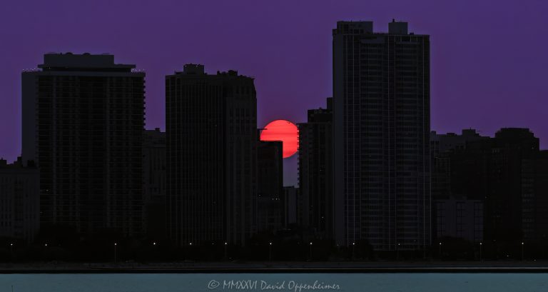 Chicago sunset between Gold Coast lakefront towers, with a fire-orange sun partly obscured by a silhouetted building edge beneath a purple sky. A gull crosses the upper rim of the solar disc, and two small sunspots appear as the sun reaches the North Lake Shore Drive skyline in Chicago, Illinois – © 2026 David Oppenheimer – Performance Impressions photography archives https://performanceimpressions.com Chicago sunset, Gold Coast sunset, Chicago skyline, Chicago cityscape, Lake Shore Drive sunset, setting sun, low sun, orange sun, purple sky, sunset sky, sun, sunset, solar disc, sunspots, solar activity, gull, seagull, bird, bird silhouette, bird in flight, skyline silhouette, building silhouettes, silhouette, horizon, summer sunset, summer, golden hour, evening, 1300 Lake Shore Drive, 1300 N Lake Shore Drive, 1300 Lake Shore condos, 1212 Lake Shore Drive, 1212 N Lake Shore Drive, 1212 Lake Shore condos, 1240 Lake Shore Drive, 1240 N Lake Shore Drive, 1240 Lake Shore condos, 1242 Lake Shore Drive, 1242 N Lake Shore Drive, 1242 Lake Shore co-op, Gold Coast, Gold Coast Chicago, Gold Coast condos, Near North Side, North Lake Shore Drive, Lake Shore Drive, DuSable Lake Shore Drive, Lake Michigan, Chicago lakefront, Chicago waterfront, Chicago, Chicago Illinois, Chicago IL, Illinois, 60610, skyline, cityscape, landscape, city, urban, buildings, towers, lakefront towers, residential towers, high rise, skyscrapers, architecture, Chicago architecture, residential architecture, lakefront architecture, condominiums, condos, co-op, residential, housing, real estate, Chicago real estate, Gold Coast real estate, lakefront real estate, sunset photography, sun photography, skyline photography, cityscape photography, landscape photography, architectural photography, Chicago art, sunset art, skyline art, city art, artwork, photo art, wall art, United States, licensing, image licensing, commercial imagery, photography licensing, art, print, fine art, commercial photography, David Oppenheimer, horizontal, 1-15213827141