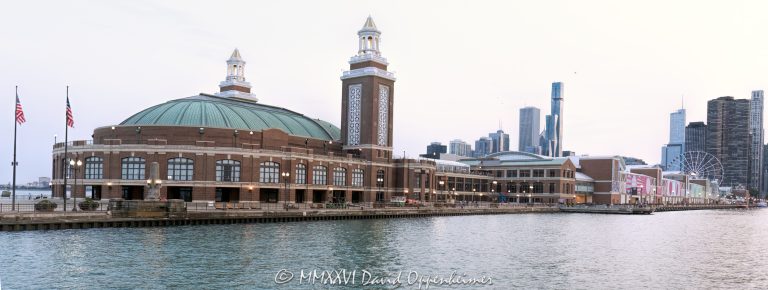 The Aon Grand Ballroom at Navy Pier, part of the pier’s original 1916 construction, fills the foreground in a Lake Michigan view toward the Chicago skyline. Its green domed roof and lantern-topped towers rise behind two flags, while the Terminal Building, Offshore Rooftop and Centennial Wheel recede along the diagonal pier beneath a pale sky in Chicago, Illinois – © 2026 David Oppenheimer – Performance Impressions photography archives https://performanceimpressions.com Navy Pier Auditorium, Aon Grand Ballroom, 600 East Grand Avenue, Navy Pier Chicago, Navy Pier Terminal Building, Navy Pier Shelter Building, Offshore Rooftop, Offshore Rooftop and Bar, Centennial Wheel, Navy Pier, auditorium exterior, ballroom exterior, building exterior, facade, architecture, Chicago Landmark, green domed roof, domed roof, twin towers, concert hall towers, lantern towers, brick facade, terra cotta, two flags, flags, flagpoles, East End Plaza, North Dock, North Dock Road, East Grand Avenue, Lake Michigan, Chicago Harbor, Chicago waterfront, Chicago lakefront, Chicago skyline, Chicago cityscape, skyline, city skyline, cityscape, skyline view, waterfront skyline, lakefront skyline, urban skyline, city view, lake view, postcard view, Chicago postcard, Navy Pier postcard, pale sky, Visit Chicago, Visit Navy Pier, Chicago tourism, Chicago travel, Chicago attractions, Chicago landmarks, things to do in Chicago, tourist attraction, travel destination, sightseeing, tourism, travel, shopping, Navy Pier shopping, dining, Navy Pier dining, Navy Pier restaurants, entertainment, Ferris wheel, Chicago Ferris wheel, observation wheel, Navy Pier Salute, World War II memorial, Bob Newhart Statue, Grand Ballroom, Municipal Pier, Municipal Pier No. 2, Charles Sumner Frost, Frost and Granger, Arts and Crafts architecture, Edward C. Shankland, William Artingstall, KOO, Maverick Hospitality, Dutch Wheels, Aon plc, Streeterville, Chicago, Illinois, Cook County, Great Lakes, USA, United States, 60611, travel photography, tourism photography, postcard photography, cityscape photography, destination imagery, landmark photography, Licensing, image licensing, commercial imagery, photography licensing, art, print, fine art, commercial photography, David Oppenheimer, horizontal, 1-15213827141