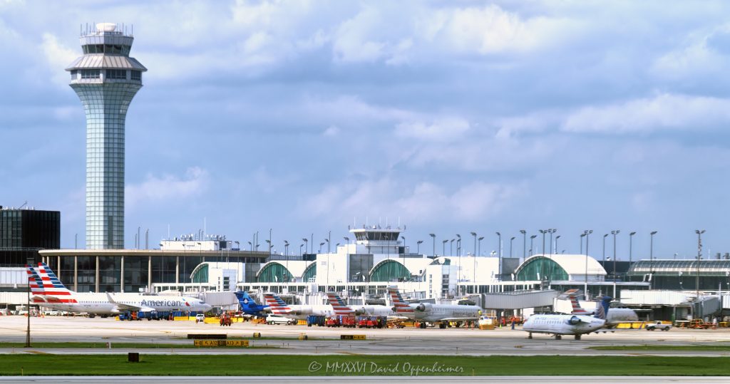ATC Tower and American Airlines Terminal 3 at Chicago O’Hare Airport in Chicago, Illinois, shown from the tarmac with aircraft, gates, jet bridges, taxiways, and terminal architecture. Daytime view of American Airlines and American Eagle operations near Terminal 3 Concourse G, including arched roof structures, commercial aircraft, and airport ramp activity – © 2026 David Oppenheimer – Performance Impressions photography archives https://performanceimpressions.com Chicago O’Hare International Airport, O’Hare International Airport, O’Hare Airport, Chicago O’Hare, O’Hare, ORD, ORD Airport, Chicago airport, airport, ATC tower, air traffic control tower, control tower, FAA tower, airport tower, American Airlines, American Airlines jets, AA, AA jets, American Eagle, aircraft, airplane, airplanes, jet, jets, passenger jet, commercial aircraft, Terminal 3, Terminal 3 Concourse G, Concourse G, terminal concourse, airport terminal, airline terminal, passenger terminal, terminal, terminal building, terminal architecture, arched roof, airport architecture, aviation, commercial aviation, airline, airlines, airport operations, airline operations, ground operations, airport ramp, ramp area, airport tarmac, tarmac, airport apron, taxiway, jet bridge, gate area, airport gate, aircraft gates, airport infrastructure, aviation infrastructure, airport scene, air travel, travel, transportation, transportation infrastructure, modern architecture, urban infrastructure, Chicago, Chicago Illinois, Illinois, United States, 60666, daytime, city airport, Midwest aviation, aviation industry, transportation hub, hub airport, O’Hare terminal, O’Hare tower, photorealism, photorealistic, digital art, artwork, rich color, saturated color, commercial photography, commercial imagery, image licensing, licensing, photography licensing, David Oppenheimer, horizontal, 1-15156784411