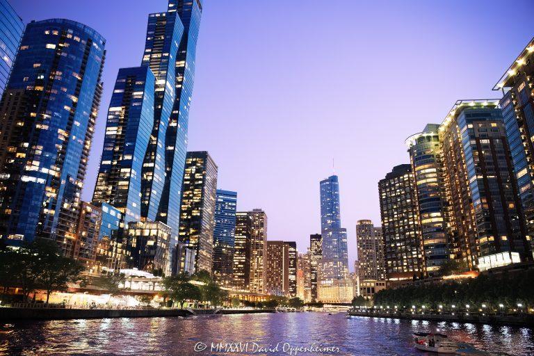 Chicago River skyline at blue hour, with illuminated towers lining both banks and city lights reflecting across the water beneath the fading post-sunset sky. The Chicago Riverwalk follows the left bank as the river bends between hotel, office, and residential towers in downtown Chicago, Illinois – © 2026 David Oppenheimer – Performance Impressions photography archives https://performanceimpressions.com
