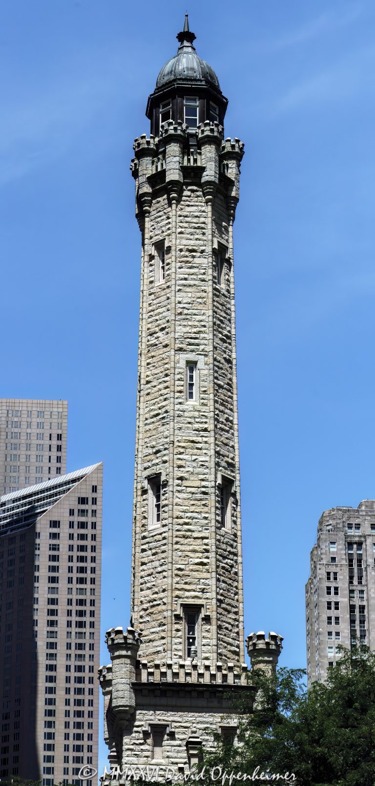 Chicago Water Tower at 806 North Michigan Avenue in Chicago, Illinois, shown in a vertical daytime view emphasizing its limestone stonework, castellated Gothic Revival detailing, turrets, pointed arches, and tower profile. Designed by William W. Boyington to house a standpipe for the Chicago Avenue waterworks system, the landmark survived the Great Chicago Fire of 1871 and remains a defining structure on the Magnificent Mile – © 2026 David Oppenheimer – Performance Impressions photography archives https://performanceimpressions.com Chicago Water Tower, Historic Chicago Water Tower, Chicago Avenue Water Tower, Chicago Avenue Water Tower and Pumping Station, 806 North Michigan Avenue, 806 N Michigan Avenue, North Michigan Avenue, Michigan Avenue, Magnificent Mile, Mag Mile, Near North Side, Streeterville, Jane M Byrne Plaza, Chicago, Chicago Illinois, Chicago IL, Illinois, 60611, facade, building exterior, exterior, tower exterior, stone facade, limestone facade, stonework, masonry, limestone, Joliet limestone, Lemont limestone, Gothic Revival, Gothic Revival architecture, castellated Gothic, historic architecture, landmark architecture, Chicago architecture, vertical architecture, architecture, architectural photography, tower, water tower, historic tower, standpipe, standpipe tower, waterworks, water supply, municipal infrastructure, infrastructure, Chicago Water Works, Chicago Avenue Pumping Station, City Gallery, City Gallery in the Historic Water Tower, Water Tower Place, Great Chicago Fire, fire survivor, Chicago history, historic landmark, Chicago Landmark, National Register of Historic Places, Old Chicago Water Tower District, American Water Landmark, William W Boyington, William Boyington, Ellis S Chesbrough, pointed arches, lancet windows, crenellations, battlements, turrets, spire, buttresses, parapet, ornate stone, daytime, daylight, tourism, travel, destination, landmark, historic, building, United States, licensing, image licensing, commercial imagery, photography licensing, art, print, fine art, commercial photography, David Oppenheimer, vertical, 1-15213827141