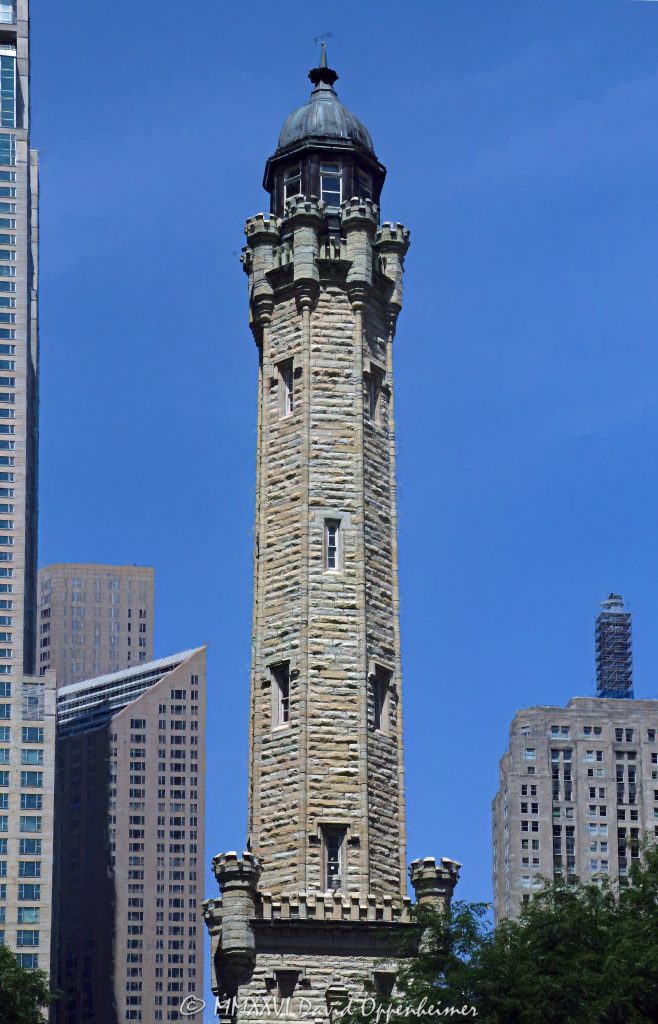Chicago Water Tower at 806 North Michigan Avenue in Chicago, Illinois, shown in a vertical daytime view emphasizing its limestone stonework, castellated Gothic Revival detailing, turrets, pointed arches, and tower profile. Designed by William W. Boyington to house a standpipe for the Chicago Avenue waterworks system, the landmark survived the Great Chicago Fire of 1871 and remains a defining structure on the Magnificent Mile – © 2026 David Oppenheimer – Performance Impressions photography archives https://performanceimpressions.com Chicago Water Tower, Historic Chicago Water Tower, Chicago Avenue Water Tower, Chicago Avenue Water Tower and Pumping Station, 806 North Michigan Avenue, 806 N Michigan Avenue, North Michigan Avenue, Michigan Avenue, Magnificent Mile, Mag Mile, Near North Side, Streeterville, Jane M Byrne Plaza, Chicago, Chicago Illinois, Chicago IL, Illinois, 60611, facade, building exterior, exterior, tower exterior, stone facade, limestone facade, stonework, masonry, limestone, Joliet limestone, Lemont limestone, Gothic Revival, Gothic Revival architecture, castellated Gothic, historic architecture, landmark architecture, Chicago architecture, vertical architecture, architecture, architectural photography, tower, water tower, historic tower, standpipe, standpipe tower, waterworks, water supply, municipal infrastructure, infrastructure, Chicago Water Works, Chicago Avenue Pumping Station, City Gallery, City Gallery in the Historic Water Tower, Water Tower Place, Great Chicago Fire, fire survivor, Chicago history, historic landmark, Chicago Landmark, National Register of Historic Places, Old Chicago Water Tower District, American Water Landmark, William W Boyington, William Boyington, Ellis S Chesbrough, pointed arches, lancet windows, crenellations, battlements, turrets, spire, buttresses, parapet, ornate stone, daytime, daylight, tourism, travel, destination, landmark, historic, building, United States, licensing, image licensing, commercial imagery, photography licensing, art, print, fine art, commercial photography, David Oppenheimer, vertical, 1-15213827141