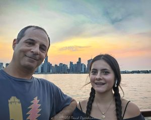 Chicago Skyline from Lake Michigan at Sunset Chicago skyline at sunset viewed from Lake Michigan, with travel photographer David Oppenheimer and his daughter appearing in the frame during a family working vacation in Chicago, Illinois – © 2026 David Oppenheimer – Performance Impressions photography archives https://performanceimpressions.com Chicago skyline, Chicago skyline sunset, Chicago city skyline, Lake Michigan, Chicago Lake Michigan, Chicago lakefront, Chicago waterfront, downtown Chicago, Chicago downtown, Chicago cityscape, Chicago skyscrapers, Chicago architecture, Chicago skyline photography, Chicago photography, Chicago travel, Chicago tourism, Chicago vacation, Chicago sunset, Lake Michigan sunset, sunset skyline, family vacation, family travel, father daughter, father and daughter, travel photographer, photographer, portrait, city skyline, cityscape, urban skyline, skyscrapers, architecture, waterfront, lakefront, Great Lakes, Chicago, Illinois, Chicago Illinois, Midwest, United States, USA, travel, tourism, vacation, family, father, daughter, horizontal, Licensing, image licensing, commercial imagery, photography licensing, art, print, fine art, commercial photography, David Oppenheimer, David Oppenheimer photography, Performance Impressions, Performance Impressions photography archives, 1-15213827141