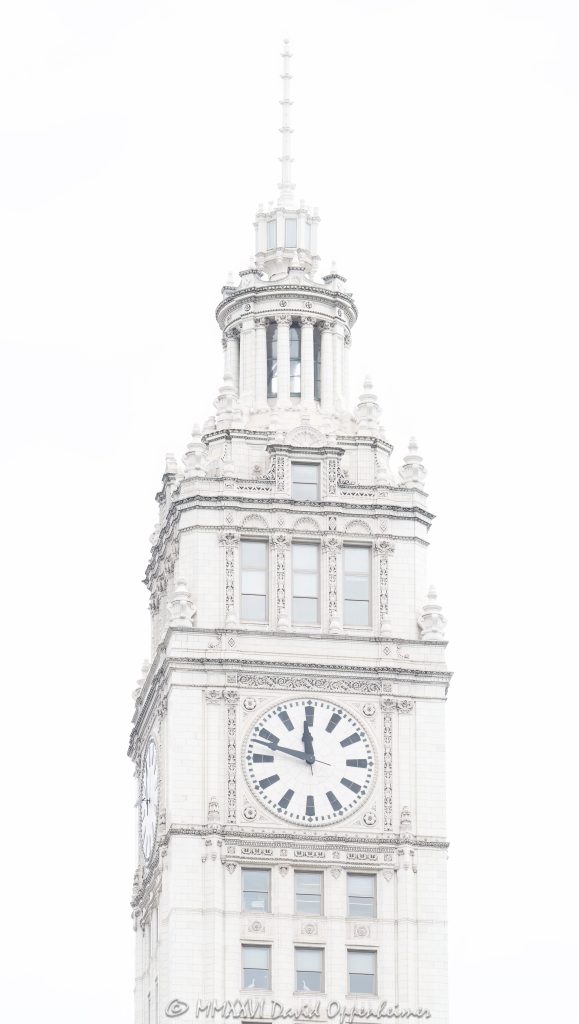 Wrigley Building clock tower at 400–410 North Michigan Avenue in Chicago, Illinois, located on the Magnificent Mile near the Chicago River. Historic terra cotta skyscraper architecture by Graham, Anderson, Probst & White featuring the building’s white clock tower, ornate facade, and landmark upper tower details. The clock reads 11:48 in this overcast close-up view of one of Chicago’s most recognizable buildings – © 2026 David Oppenheimer – Performance Impressions photography archives https://performanceimpressions.com Wrigley Building, Wrigley Building Chicago, Wrigley clock tower, Wrigley Building clock tower, clock tower, building clock, 400 North Michigan, 400 North Michigan Avenue, 410 North Michigan, 410 North Michigan Avenue, 400 N Michigan, 410 N Michigan, North Michigan Avenue, Michigan Avenue, Magnificent Mile, Chicago, Chicago Illinois, Illinois, United States, 60611, Downtown Chicago, Near North Side, Chicago Loop, Chicago River, architecture, Chicago architecture, architectural photography, facade, building exterior, exterior, historic architecture, terra cotta, white terra cotta, terra cotta facade, white facade, ornate facade, clock face, 11:48, tower detail, upper tower, landmark building, Chicago Landmark, historic building, skyscraper, high-rise, building, tower, office building, commercial building, commercial real estate, corporate real estate, real estate, Beaux-Arts architecture, Spanish Revival, French Renaissance, Graham Anderson Probst White, Graham Anderson Probst and White, GAPW, William Wrigley Jr, Wrigley Company, chewing gum company, Tribune Tower, DuSable Bridge, Michigan Avenue Bridge, white building, overcast, cloudy sky, soft light, daylight, urban architecture, American architecture, Illinois architecture, downtown, urban, tourism, travel, Chicago landmark, iconic building, commercial photography, commercial imagery, image licensing, licensing, photography licensing, art, print, fine art, David Oppenheimer, vertical, 1-15156784411