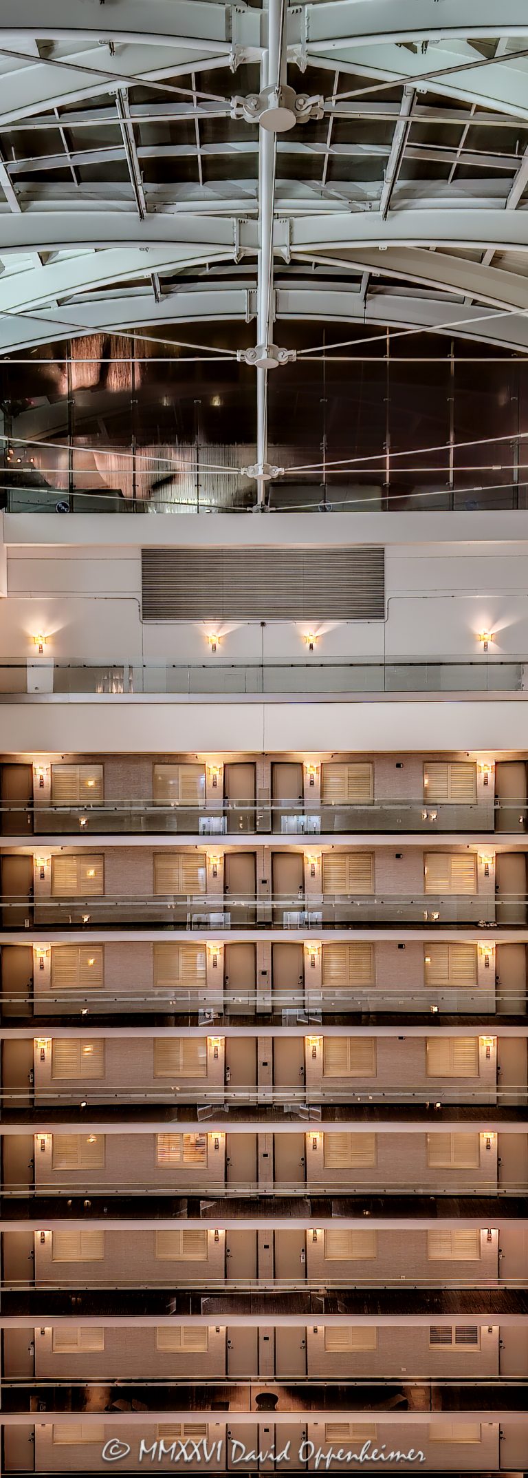 Embassy Suites by Hilton Chicago Downtown Magnificent Mile atrium interior in Chicago, Illinois, showing approximately eight upper levels of stacked guestroom corridors across the vast open interior, with strong horizontal and vertical lines rising to the curved steel framing and glazed roof structure above – © 2026 David Oppenheimer – Performance Impressions photography archives https://performanceimpressions.com Embassy Suites by Hilton Chicago Downtown Magnificent Mile, Embassy Suites Chicago Downtown Magnificent Mile, Embassy Suites Chicago Magnificent Mile, Embassy Suites Magnificent Mile, Embassy Suites Chicago, Embassy Suites by Hilton, Embassy Suites, Embassy Suites atrium, Embassy Suites interior, Chicago Embassy Suites, 511 North Columbus Drive, 511 N Columbus Drive, 511 N Columbus Dr, 60611, hotel atrium, atrium interior, Chicago hotel atrium, Chicago hotel interior, hotel interior, atrium architecture, interior architecture, hotel architecture, open atrium, multi-story atrium, tall atrium, soaring atrium, glass atrium, atrium roof, vaulted atrium, vaulted roof, glass roof, metal roof, roof structure, roof framing, roof glazing, skylight, skylight roof, steel framing, structural steel, steel beams, steel girders, arched beams, steel arches, curved steel, curved beams, roof girders, tension rods, structural rods, support cables, structural cables, horizontal lines, vertical lines, linear geometry, architectural geometry, geometric architecture, repeating lines, repetition, architectural pattern, guest corridors, guestroom corridors, hotel corridors, interior corridors, open corridors, atrium corridors, upper floors, hotel floors, guestroom doors, interior walkways, structural engineering, engineering, architectural engineering, structural design, building structure, steel structure, hospitality architecture, hospitality design, interior design, commercial interior, commercial architecture, high-rise hotel, hotel tower, all-suite hotel, all suite hotel, upscale hotel, full service hotel, Chicago hotel, downtown Chicago hotel, Streeterville hotel, Magnificent Mile hotel, Chicago hospitality, Streeterville, River East, River East Chicago, River East Center, Magnificent Mile, downtown Chicago, Near North Side, Chicago, Chicago Illinois, Illinois, United States, USA, Embassy Suites Chicago Downtown-Lakefront, Embassy Suites Downtown Lakefront, Chicago Downtown Lakefront, DeStefano + Partners, DeStefano and Partners, DeStefano Partners, Greg Randall, architect, architecture firm, The Gettys Group, Gettys Group, Gettys, interior designer, MCL Companies, MCL, developer, Hilton, Hilton Worldwide, Hilton Worldwide Holdings, HLT, NYSE HLT, Hilton stock, Host Hotels & Resorts, Host Hotels, Host Hotels and Resorts, HST, NASDAQ HST, hotel REIT, hospitality, hotel, atrium, interior, architecture, structure, steel, glass, glazing, Art Deco, Art Deco influence, contemporary design, architectural photography, interior photography, hotel photography, Chicago architecture photography, structural photography, fine art photography, architectural print, photographic print, archival print, gallery print, collector print, wall art, Chicago architecture art, licensing, image licensing, commercial imagery, photography licensing, art, print, fine art, commercial photography, David Oppenheimer, David Oppenheimer photography, Performance Impressions, Performance Impressions photography archives, vertical, 1-15213827141
