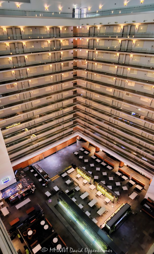 Elevated view across the atrium interior of Embassy Suites by Hilton Chicago Downtown Magnificent Mile in Streeterville, Chicago, Illinois, looking down from an upper level toward the hotel’s lower dining and public areas. Approximately twelve visible levels of open guestroom corridors extend around the vast central atrium, with angled walkways meeting at a corner and repeating railings, floor edges, horizontal lines and diagonal geometry defining the multi-story interior – © 2026 David Oppenheimer – Performance Impressions photography archives https://performanceimpressions.com Embassy Suites by Hilton Chicago Downtown Magnificent Mile, Embassy Suites Chicago Downtown Magnificent Mile, Embassy Suites Chicago Magnificent Mile, Embassy Suites Magnificent Mile, Embassy Suites Chicago, Embassy Suites by Hilton, Embassy Suites, Chicago Embassy Suites, 511 North Columbus Drive, 511 N Columbus Drive, 511 N Columbus Dr, 60611, Embassy Suites atrium, Embassy Suites interior, hotel atrium, Chicago hotel atrium, atrium interior, Chicago hotel interior, hotel interior, elevated atrium view, elevated view, upper floor view, high angle view, atrium overview, atrium view, looking down, open atrium, central atrium, multi-story atrium, multistory atrium, multi-level atrium, tall atrium, large atrium, vast atrium, vast interior, open interior, open volume, atrium architecture, interior architecture, hotel architecture, hospitality architecture, hospitality design, interior design, commercial interior, commercial architecture, guestroom corridors, guest corridors, hotel corridors, atrium corridors, open corridors, gallery corridors, interior corridors, hotel hallways, interior hallways, walkways, interior walkways, open walkways, angled walkways, diagonal walkways, corner walkways, intersecting corridors, corridor junction, stacked corridors, stacked floors, multiple floors, multiple levels, upper floors, hotel floors, guestroom levels, guestroom doors, room doors, railings, corridor railings, floor edges, atrium floor, lower floor, lower level, main level, hotel dining, dining area, dining space, hotel dining area, public areas, public space, common areas, seating area, hotel interior space, horizontal lines, vertical lines, diagonal lines, angled lines, converging lines, repeating lines, architectural lines, linear architecture, linear geometry, architectural geometry, geometric architecture, geometric interior, geometric design, corner geometry, repeating geometry, architectural pattern, repetition, pattern, symmetry, perspective, elevated perspective, interior perspective, depth, spatial depth, architectural depth, abstract architecture, architectural abstraction, geometric abstraction, abstract interior, architectural abstract, modern geometry, structural geometry, interior structure, building structure, structural design, structural engineering, architectural engineering, engineering, contemporary architecture, contemporary interior, contemporary design, Art Deco, Art Deco architecture, Art Deco interior, Art Deco influence, modern Art Deco, retro, retro design, retro interior, 2000s architecture, hotel design, all-suite hotel, all suite hotel, upscale hotel, full service hotel, Chicago hotel, downtown Chicago hotel, Magnificent Mile hotel, Streeterville hotel, Chicago hospitality, Streeterville, River East, River East Chicago, Magnificent Mile, downtown Chicago, Near North Side, Columbus Drive, Chicago, Chicago Illinois, Illinois, United States, USA, Embassy Suites Chicago Downtown-Lakefront, Embassy Suites Downtown Lakefront, Chicago Downtown Lakefront, DeStefano + Partners, DeStefano and Partners, DeStefano Partners, Greg Randall, architect, architects, architecture firm, The Gettys Group, Gettys Group, Gettys, interior designer, MCL Companies, MCL, developer, Hilton, Hilton Hotels, Hilton Worldwide, Hilton Worldwide Holdings, HLT, NYSE HLT, Hilton stock, Host Hotels & Resorts, Host Hotels, Host Hotels and Resorts, HST, NASDAQ HST, hotel REIT, hospitality, hotel, atrium, interior, architecture, structure, geometry, geometric, corridors, hallway, walkways, railings, architectural photography, interior photography, hotel photography, atrium photography, geometric photography, abstract photography, Chicago architecture photography, structural photography, fine art photography, architectural print, photographic print, archival print, gallery print, collector print, wall art, Chicago architecture art, hotel art, atrium art, abstract art, geometric art, licensing, image licensing, commercial imagery, photography licensing, art, print, fine art, commercial photography, David Oppenheimer, David Oppenheimer photography, Performance Impressions, Performance Impressions photography archives, horizontal, 1-15213827141