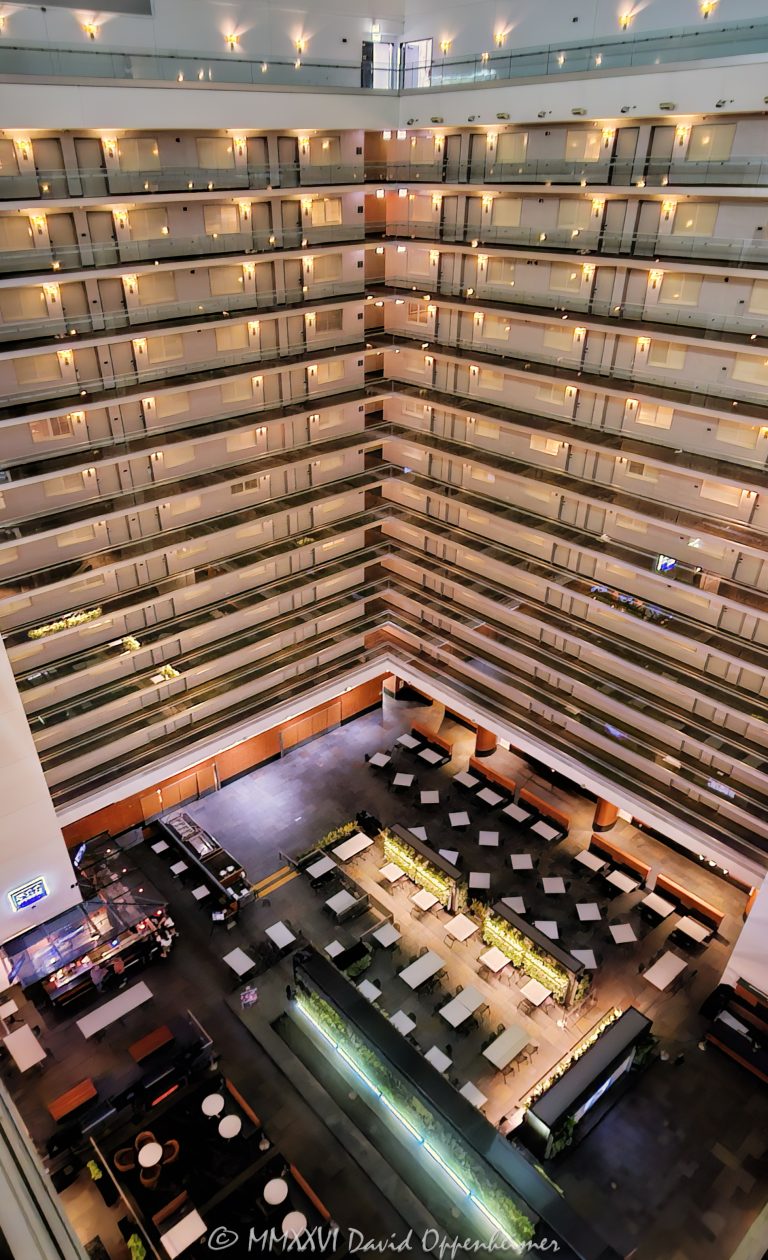 Elevated view across the atrium interior of Embassy Suites by Hilton Chicago Downtown Magnificent Mile in Streeterville, Chicago, Illinois, looking down from an upper level toward the hotel’s lower dining and public areas. Approximately twelve visible levels of open guestroom corridors extend around the vast central atrium, with angled walkways meeting at a corner and repeating railings, floor edges, horizontal lines and diagonal geometry defining the multi-story interior – © 2026 David Oppenheimer – Performance Impressions photography archives https://performanceimpressions.com Embassy Suites by Hilton Chicago Downtown Magnificent Mile, Embassy Suites Chicago Downtown Magnificent Mile, Embassy Suites Chicago Magnificent Mile, Embassy Suites Magnificent Mile, Embassy Suites Chicago, Embassy Suites by Hilton, Embassy Suites, Chicago Embassy Suites, 511 North Columbus Drive, 511 N Columbus Drive, 511 N Columbus Dr, 60611, Embassy Suites atrium, Embassy Suites interior, hotel atrium, Chicago hotel atrium, atrium interior, Chicago hotel interior, hotel interior, elevated atrium view, elevated view, upper floor view, high angle view, atrium overview, atrium view, looking down, open atrium, central atrium, multi-story atrium, multistory atrium, multi-level atrium, tall atrium, large atrium, vast atrium, vast interior, open interior, open volume, atrium architecture, interior architecture, hotel architecture, hospitality architecture, hospitality design, interior design, commercial interior, commercial architecture, guestroom corridors, guest corridors, hotel corridors, atrium corridors, open corridors, gallery corridors, interior corridors, hotel hallways, interior hallways, walkways, interior walkways, open walkways, angled walkways, diagonal walkways, corner walkways, intersecting corridors, corridor junction, stacked corridors, stacked floors, multiple floors, multiple levels, upper floors, hotel floors, guestroom levels, guestroom doors, room doors, railings, corridor railings, floor edges, atrium floor, lower floor, lower level, main level, hotel dining, dining area, dining space, hotel dining area, public areas, public space, common areas, seating area, hotel interior space, horizontal lines, vertical lines, diagonal lines, angled lines, converging lines, repeating lines, architectural lines, linear architecture, linear geometry, architectural geometry, geometric architecture, geometric interior, geometric design, corner geometry, repeating geometry, architectural pattern, repetition, pattern, symmetry, perspective, elevated perspective, interior perspective, depth, spatial depth, architectural depth, abstract architecture, architectural abstraction, geometric abstraction, abstract interior, architectural abstract, modern geometry, structural geometry, interior structure, building structure, structural design, structural engineering, architectural engineering, engineering, contemporary architecture, contemporary interior, contemporary design, Art Deco, Art Deco architecture, Art Deco interior, Art Deco influence, modern Art Deco, retro, retro design, retro interior, 2000s architecture, hotel design, all-suite hotel, all suite hotel, upscale hotel, full service hotel, Chicago hotel, downtown Chicago hotel, Magnificent Mile hotel, Streeterville hotel, Chicago hospitality, Streeterville, River East, River East Chicago, Magnificent Mile, downtown Chicago, Near North Side, Columbus Drive, Chicago, Chicago Illinois, Illinois, United States, USA, Embassy Suites Chicago Downtown-Lakefront, Embassy Suites Downtown Lakefront, Chicago Downtown Lakefront, DeStefano + Partners, DeStefano and Partners, DeStefano Partners, Greg Randall, architect, architects, architecture firm, The Gettys Group, Gettys Group, Gettys, interior designer, MCL Companies, MCL, developer, Hilton, Hilton Hotels, Hilton Worldwide, Hilton Worldwide Holdings, HLT, NYSE HLT, Hilton stock, Host Hotels & Resorts, Host Hotels, Host Hotels and Resorts, HST, NASDAQ HST, hotel REIT, hospitality, hotel, atrium, interior, architecture, structure, geometry, geometric, corridors, hallway, walkways, railings, architectural photography, interior photography, hotel photography, atrium photography, geometric photography, abstract photography, Chicago architecture photography, structural photography, fine art photography, architectural print, photographic print, archival print, gallery print, collector print, wall art, Chicago architecture art, hotel art, atrium art, abstract art, geometric art, licensing, image licensing, commercial imagery, photography licensing, art, print, fine art, commercial photography, David Oppenheimer, David Oppenheimer photography, Performance Impressions, Performance Impressions photography archives, horizontal, 1-15213827141