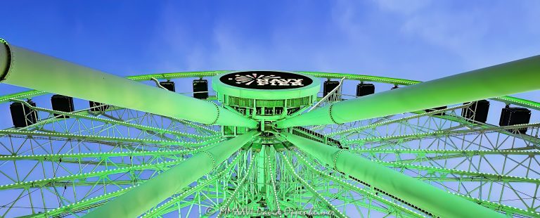 Navy Pier Centennial Wheel in Chicago, Illinois, viewed from below at blue hour with the Ferris wheel illuminated green and the Navy Pier logo visible at the center hub. Angled steel support legs, spokes and the circular wheel structure create a strong geometric view of the Dutch Wheels-designed attraction at Pier Park on the Chicago lakefront – © 2026 David Oppenheimer – Performance Impressions photography archives https://performanceimpressions.com Centennial Wheel, Navy Pier Centennial Wheel, Centennial Ferris Wheel, Centennial Wheel Chicago, Centennial Wheel Navy Pier, Navy Pier wheel, Navy Pier Ferris Wheel, Chicago Ferris wheel, Chicago wheel, Ferris wheel, observation wheel, giant wheel, wheel, Navy Pier, Navy Pier Chicago, Chicago Navy Pier, Pier Park, Navy Pier Pier Park, Ferris wheel ride, amusement ride, attraction, Chicago attraction, tourist attraction, Chicago landmark, lakefront attraction, Navy Pier logo, Navy Pier sign, center hub, wheel hub, digital hub, spokes, wheel spokes, gondolas, enclosed gondolas, passenger gondolas, support legs, wheel supports, steel supports, steel legs, steel beams, steel structure, structural steel, wheel structure, engineering, structural engineering, geometry, geometric, radial geometry, radial lines, circular, circle, symmetry, green, green lights, green lighting, green illumination, illuminated, illumination, lighting, blue hour, twilight, evening, low angle, looking up, upward view, dramatic perspective, architectural perspective, Streeterville, Streeterville Chicago, Near North Side, Chicago lakefront, Chicago waterfront, lakefront, waterfront, Lake Michigan, Grand Avenue, 600 East Grand Avenue, 600 E Grand Ave, 60611, Chicago, Chicago Illinois, Illinois, United States, USA, Dutch Wheels, Dutch Wheels BV, Netherlands, Navy Pier Inc, amusement, recreation, tourism, Chicago tourism, Chicago travel, entertainment, family attraction, outdoor attraction, city lights, night photography, blue hour photography, Ferris wheel photography, Navy Pier photography, Chicago photography, architectural photography, structural photography, travel photography, editorial photography, fine art photography, Chicago art, Navy Pier art, Ferris wheel art, photographic print, architectural print, fine art print, archival print, gallery print, collector print, wall art, licensing, image licensing, commercial imagery, photography licensing, art, print, fine art, commercial photography, David Oppenheimer, Performance Impressions, Performance Impressions photography archives, horizontal, 1-15213827141