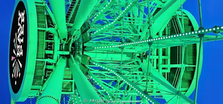 Navy Pier Centennial Wheel in Chicago, Illinois, viewed from below at blue hour with the Ferris wheel illuminated green and the Navy Pier logo visible at the center hub. Angled steel support legs, spokes and the circular wheel structure create a strong geometric view of the Dutch Wheels-designed attraction at Pier Park on the Chicago lakefront – © 2026 David Oppenheimer – Performance Impressions photography archives https://performanceimpressions.com Centennial Wheel, Navy Pier Centennial Wheel, Centennial Ferris Wheel, Centennial Wheel Chicago, Centennial Wheel Navy Pier, Navy Pier wheel, Navy Pier Ferris Wheel, Chicago Ferris wheel, Chicago wheel, Ferris wheel, observation wheel, giant wheel, wheel, Navy Pier, Navy Pier Chicago, Chicago Navy Pier, Pier Park, Navy Pier Pier Park, Ferris wheel ride, amusement ride, attraction, Chicago attraction, tourist attraction, Chicago landmark, lakefront attraction, Navy Pier logo, Navy Pier sign, center hub, wheel hub, digital hub, spokes, wheel spokes, gondolas, enclosed gondolas, passenger gondolas, support legs, wheel supports, steel supports, steel legs, steel beams, steel structure, structural steel, wheel structure, engineering, structural engineering, geometry, geometric, radial geometry, radial lines, circular, circle, symmetry, green, green lights, green lighting, green illumination, illuminated, illumination, lighting, blue hour, twilight, evening, low angle, looking up, upward view, dramatic perspective, architectural perspective, Streeterville, Streeterville Chicago, Near North Side, Chicago lakefront, Chicago waterfront, lakefront, waterfront, Lake Michigan, Grand Avenue, 600 East Grand Avenue, 600 E Grand Ave, 60611, Chicago, Chicago Illinois, Illinois, United States, USA, Dutch Wheels, Dutch Wheels BV, Netherlands, Navy Pier Inc, amusement, recreation, tourism, Chicago tourism, Chicago travel, entertainment, family attraction, outdoor attraction, city lights, night photography, blue hour photography, Ferris wheel photography, Navy Pier photography, Chicago photography, architectural photography, structural photography, travel photography, editorial photography, fine art photography, Chicago art, Navy Pier art, Ferris wheel art, photographic print, architectural print, fine art print, archival print, gallery print, collector print, wall art, licensing, image licensing, commercial imagery, photography licensing, art, print, fine art, commercial photography, David Oppenheimer, Performance Impressions, Performance Impressions photography archives, horizontal, 1-15213827141