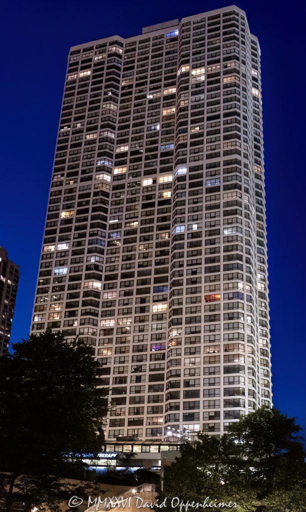River Plaza Condominiums at 405 North Wabash Avenue rises above River North against a purple post-sunset sky, with illuminated windows forming a geometric pattern across its glass-and-concrete facade. Designed by Gordon & Levin and later converted from rental apartments to condominiums, the residential tower stands near the Chicago River in Chicago, Illinois – © 2026 David Oppenheimer – Performance Impressions photography archives https://performanceimpressions.com River Plaza Condominiums, River Plaza, River Plaza Chicago, River Plaza condos, River Plaza Tower, 405 North Wabash Avenue, 405 N Wabash Avenue, 405 N Wabash Ave, 405 North Wabash, North Wabash Avenue, Wabash Avenue, River North, River North Chicago, Near North Side, downtown Chicago, Chicago River, Chicago Riverwalk, Riverwalk, riverfront, Michigan Avenue, Magnificent Mile, Wrigley Building, Chicago, Chicago Illinois, Chicago IL, Illinois, 60611, facade, building exterior, exterior, tower exterior, glass facade, concrete facade, glass and concrete, window facade, window grid, illuminated facade, illuminated windows, building lights, window lights, facade lighting, geometric facade, facade pattern, window pattern, grid pattern, architectural pattern, reflections, purple sky, purple twilight, twilight, dusk, after sunset, evening, evening light, city lights, Chicago twilight, Chicago evening, condominium tower, condo tower, residential tower, residential high rise, residential skyscraper, condominium building, residential building, condominiums, condos, Chicago condos, River North condos, downtown condos, luxury condos, urban condos, high rise, skyscraper, tower, building, concrete tower, glass tower, housing, multifamily, former apartments, apartment conversion, condo conversion, real estate, River Plaza real estate, Chicago real estate, River North real estate, condominium real estate, condo real estate, residential real estate, downtown real estate, riverfront real estate, architecture, architectural photography, Chicago architecture, residential architecture, high-rise architecture, modern architecture, modernist architecture, postwar architecture, concrete architecture, structural engineering, high-strength concrete, reinforced concrete, Gordon & Levin, Gordon and Levin, Ezra Gordon, Jack M Levin, Margaret Young, McHugh Construction, James McHugh Construction, H S Nachman Associates, Field Enterprises, Community Specialists, Chicago skyline, urban architecture, city living, urban living, city views, river views, United States, licensing, image licensing, commercial imagery, photography licensing, art, print, fine art, commercial photography, David Oppenheimer, vertical, 1-15213827141