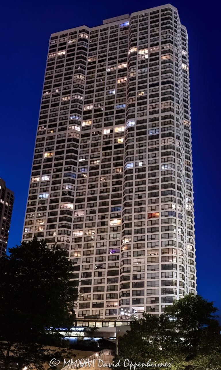 River Plaza Condominiums at 405 North Wabash Avenue rises above River North against a purple post-sunset sky, with illuminated windows forming a geometric pattern across its glass-and-concrete facade. Designed by Gordon & Levin and later converted from rental apartments to condominiums, the residential tower stands near the Chicago River in Chicago, Illinois – © 2026 David Oppenheimer – Performance Impressions photography archives https://performanceimpressions.com River Plaza Condominiums, River Plaza, River Plaza Chicago, River Plaza condos, River Plaza Tower, 405 North Wabash Avenue, 405 N Wabash Avenue, 405 N Wabash Ave, 405 North Wabash, North Wabash Avenue, Wabash Avenue, River North, River North Chicago, Near North Side, downtown Chicago, Chicago River, Chicago Riverwalk, Riverwalk, riverfront, Michigan Avenue, Magnificent Mile, Wrigley Building, Chicago, Chicago Illinois, Chicago IL, Illinois, 60611, facade, building exterior, exterior, tower exterior, glass facade, concrete facade, glass and concrete, window facade, window grid, illuminated facade, illuminated windows, building lights, window lights, facade lighting, geometric facade, facade pattern, window pattern, grid pattern, architectural pattern, reflections, purple sky, purple twilight, twilight, dusk, after sunset, evening, evening light, city lights, Chicago twilight, Chicago evening, condominium tower, condo tower, residential tower, residential high rise, residential skyscraper, condominium building, residential building, condominiums, condos, Chicago condos, River North condos, downtown condos, luxury condos, urban condos, high rise, skyscraper, tower, building, concrete tower, glass tower, housing, multifamily, former apartments, apartment conversion, condo conversion, real estate, River Plaza real estate, Chicago real estate, River North real estate, condominium real estate, condo real estate, residential real estate, downtown real estate, riverfront real estate, architecture, architectural photography, Chicago architecture, residential architecture, high-rise architecture, modern architecture, modernist architecture, postwar architecture, concrete architecture, structural engineering, high-strength concrete, reinforced concrete, Gordon & Levin, Gordon and Levin, Ezra Gordon, Jack M Levin, Margaret Young, McHugh Construction, James McHugh Construction, H S Nachman Associates, Field Enterprises, Community Specialists, Chicago skyline, urban architecture, city living, urban living, city views, river views, United States, licensing, image licensing, commercial imagery, photography licensing, art, print, fine art, commercial photography, David Oppenheimer, vertical, 1-15213827141