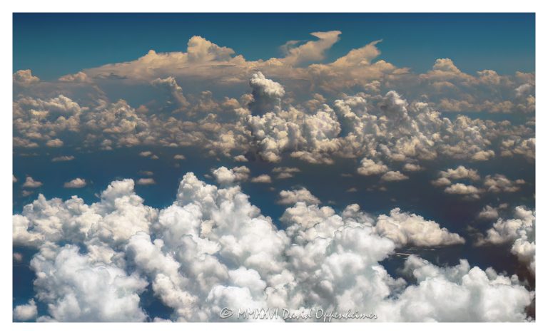Towering summer clouds aerial photo showing cumulus congestus clouds, developing cumulonimbus formations, and broad convective cloud fields rising above darker atmospheric haze and blue sky. Sunlit cloud tops, vertical cloud towers, and expanding storm structure emphasize summer weather, atmospheric instability, and high-altitude meteorology – © 2026 David Oppenheimer – Performance Impressions aerial photography archives https://performanceimpressions.com towering summer clouds, summer clouds aerial photo, towering clouds, clouds aerial view, aerial clouds, cloudscape, cloudscape aerial, cloud formations, cloud towers, cloud tops, towering cumulus, cumulus clouds, cumulus, cumulus congestus, developing cumulonimbus, cumulonimbus clouds, thunderstorm clouds, storm clouds, convective clouds, convection, atmospheric convection, weather, meteorology, atmosphere, atmospheric, sky, blue sky, white clouds, dramatic clouds, towering cloudscape, cloud texture, cloud structure, cloud field, cloud cover, cloud mass, atmospheric haze, weather pattern, weather system, storm development, thunderstorm development, unstable atmosphere, summer weather, moisture, humidity, vapor, water vapor, aerial, aerial photo, aerial photography, aerial photographer, aerial view, aerial image, high altitude, altitude, aviation, airplane view, flight, travel, nature, outdoors, environment, climate, climate imagery, scenic sky, sky photography, natural pattern, weather science, meteorological, United States, licensing, image licensing, commercial imagery, photography licensing, art, print, fine art, commercial photography, David Oppenheimer, horizontal, 1-15156784411