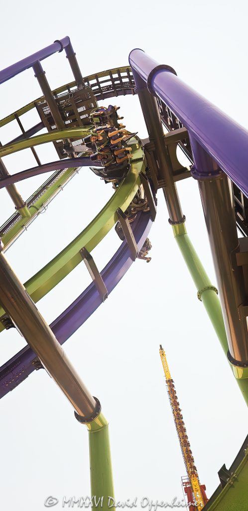 THE JOKER Free-Fly Coaster at Six Flags Great America near Chicago in Gurnee, Illinois, shown in close-up with The Joker character theming in the foreground and a coaster car flipping overhead on the attraction’s green-and-purple track. The DC Universe thrill ride is an S&S Worldwide 4D Free Spin coaster using exposed wing seating and magnetic spin-control technology to rotate riders head-over-heels – © 2026 David Oppenheimer – Performance Impressions photography archives https://performanceimpressions.com THE JOKER Free-Fly Coaster, THE JOKER Free Fly Coaster, Joker Free-Fly Coaster, Joker Free Fly Coaster, THE JOKER, The Joker, Joker, Joker coaster, Joker roller coaster, Joker ride, Six Flags Joker, Joker Six Flags, Six Flags Great America Joker, Great America Joker, Joker Chicago, Joker Illinois, DC Joker, DC Comics Joker, Joker character, Joker figure, Joker theming, Joker theme, Joker display, Joker face, Joker sign, Joker signage, supervillain, DC supervillain, villain, comic villain, comic book villain, comic character, DC Comics, DC, DC Universe, Six Flags DC Universe, DC Universe Six Flags, Great America DC Universe, DC Universe Chicago, DC Universe Illinois, roller coaster, roller coasters, coaster, coasters, steel coaster, steel roller coaster, 4D coaster, 4D roller coaster, 4D Free Spin, 4D Free Spin coaster, S&S 4D Free Spin, free spin, free-spin coaster, free fly, free-fly coaster, freestyle coaster, thrill coaster, thrill ride, thrill rides, amusement ride, theme park ride, ride, rides, coaster car, coaster vehicle, ride vehicle, winged vehicle, winged seats, wing seating, exposed seating, spinning coaster, spinning vehicle, flipping coaster, flipping riders, head-over-heels, head over heels, flips, flipping, spin, spinning, rotation, rotating seats, inversions, inversion, weightlessness, free fall, freefall, 90-degree hill, vertical lift, coaster track, roller coaster track, track, stacked track, overhead track, overhead coaster, coaster overhead, riders overhead, green track, purple track, green and purple, amusement park, theme park, amusement parks, theme parks, amusement park attraction, theme park attraction, coaster attraction, park attraction, attraction, attractions, themed attraction, themed entertainment, themed design, comic-book theme, comic theme, S&S Worldwide, S&S, S and S Worldwide, S&S Worldwide Inc, S&S coaster, S&S roller coaster, coaster manufacturer, ride manufacturer, amusement manufacturer, ride engineering, coaster engineering, engineering, engineer, amusement engineering, magnetic spin control, magnetic spin, magnetic technology, spin control, magnetic braking, eddy current, eddy current brake, ride technology, coaster technology, Todd Snyder, Mike Worley, Alan Schilke, coaster designer, ride designer, amusement design, Bleck & Bleck Architects, Bleck and Bleck Architects, Bleck Architects, Bleck & Bleck, theme park architect, theme park architecture, architect, architects, architecture, architectural design, theme park design, ride integration, attraction integration, theme integration, concept integration, land planning, marquee design, lighting design, ride structures, structural design, control systems, control integration, electrical integration, Yankee Harbor, Six Flags Yankee Harbor, DC Universe, Six Flags Great America, Six Flags Great America Chicago, Great America Chicago, Great America Illinois, Six Flags Chicago, Six Flags Illinois, Six Flags, Great America, Gurnee, Gurnee Illinois, Gurnee IL, Illinois, Lake County, Lake County Illinois, northern Illinois, Chicagoland, Chicago area, Chicago, Chicago Illinois, Chicago theme park, Chicago amusement park, Chicago attraction, Chicago attractions, Chicago tourism, Chicago travel, Visit Chicago, Illinois attraction, Illinois attractions, Illinois tourism, Illinois travel, Visit Illinois, Midwest, Midwest attraction, Midwest amusement park, Midwest theme park, Great America Parkway, 1 Great America Parkway, Grand Avenue, Route 132, Interstate 94, I-94, 60031, United States, USA, Six Flags Entertainment Corporation, Six Flags Entertainment, Six Flags company, Six Flags stock, FUN, NYSE FUN, Sansei Technologies, Sansei Group, Sansei, TSE 6357, 6357, amusement park photography, theme park photography, roller coaster photography, coaster photography, thrill ride photography, action photography, Joker photography, DC photography, entertainment photography, travel photography, tourism photography, editorial photography, commercial photography, fine art photography, amusement park art, theme park art, roller coaster art, Joker art, DC art, Six Flags art, Great America art, Chicago art, roller coaster print, Joker print, Six Flags print, Great America print, photographic print, fine art print, archival print, gallery print, collector print, wall art, licensing, image licensing, commercial imagery, photography licensing, art, print, fine art, commercial photography, David Oppenheimer, Performance Impressions, Performance Impressions photography archives, 1-15156784411