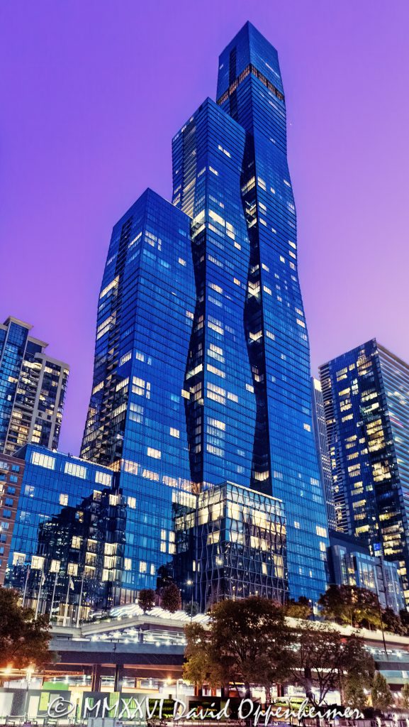 The St. Regis Chicago at 401 East Upper Wacker Drive rises above Lakeshore East at twilight, its illuminated windows articulating three interconnected volumes of blue-green glass against a purple post-sunset sky. Viewed from the Chicago River, the 101-story luxury hotel and condominium tower designed by Jeanne Gang of Studio Gang forms a sculptural landmark near Lake Michigan in Chicago, Illinois – © 2026 David Oppenheimer – Performance Impressions photography archives https://performanceimpressions.com The St. Regis Chicago, St. Regis Chicago, The St. Regis Chicago Hotel, St. Regis Hotel Chicago, The Residences at The St. Regis Chicago, St. Regis Chicago Residences, St. Regis Hotels & Resorts, 401 East Upper Wacker Drive, 401 E Upper Wacker Drive, 401 E Upper Wacker Dr, 401 East Wacker Drive, 401 E Wacker Drive, 363 East Wacker Drive, 363 E Wacker Drive, Vista Tower, Vista Tower Chicago, Wanda Vista Tower, Lakeshore East, Lakeshore East Chicago, New Eastside, Chicago Loop, Loop Chicago, downtown Chicago, East Wacker Drive, Upper Wacker Drive, Wacker Drive, Chicago River, Chicago Riverwalk, Riverwalk, riverfront, Lake Michigan, Chicago lakefront, DuSable Harbor, Navy Pier, Millennium Park, Chicago, Chicago Illinois, Chicago IL, Illinois, 60601, facade, building exterior, exterior, tower exterior, upper tower, glass facade, glass tower, glass towers, glass skyscraper, glass curtain wall, curtain wall, blue-green glass, gradient glass, aqua glass, reflective glass, high-performance glass, faceted facade, sculptural facade, geometric facade, three-volume tower, interconnected volumes, three towers, stacked frustums, frustum geometry, truncated pyramids, stepped edges, tapered tower, illuminated facade, illuminated windows, building lights, window lights, facade lighting, city lights, reflections, twilight, Chicago twilight, purple twilight, purple sky, post-sunset sky, dusk, after sunset, evening, skyline lights, luxury hotel, five-star hotel, Chicago hotel, Chicago luxury hotel, downtown hotel, riverfront hotel, Lake Michigan hotel, Marriott hotel, hotel tower, hotel, hospitality, luxury hospitality, St. Regis Butler Service, Marriott International, Marriott Bonvoy, Marriott stock, NASDAQ MAR, MAR stock, mixed-use tower, mixed-use building, condominium tower, residential tower, condominiums, luxury condos, luxury residences, Chicago condos, Lakeshore East condos, skyscraper, supertall, high rise, tower, building, 101-story tower, Chicago skyline, Chicago cityscape, skyline, cityscape, urban, city views, river views, lake views, real estate, Chicago real estate, Lakeshore East real estate, hotel real estate, hospitality real estate, condominium real estate, residential real estate, luxury real estate, riverfront real estate, commercial real estate, contemporary architecture, modern architecture, sculptural architecture, geometric architecture, high-rise architecture, riverfront architecture, Chicago architecture, architectural photography, architecture, engineering, structural engineering, wind engineering, reinforced concrete, blow-through floor, tuned liquid dampers, Studio Gang, Jeanne Gang, bKL Architecture, bKL Architects, Gensler, HBA, Magnusson Klemencic Associates, MKA, McHugh Construction, Power Construction, OLIN, Magellan Development Group, Gencom, GD Holdings, Gencom GD Holdings, hotel ownership, hotel investment, boat view, river view, Chicago River cruise, architecture cruise, urban photography, twilight photography, hotel photography, United States, licensing, image licensing, commercial imagery, photography licensing, art, print, fine art, commercial photography, David Oppenheimer, vertical, 1-15213827141