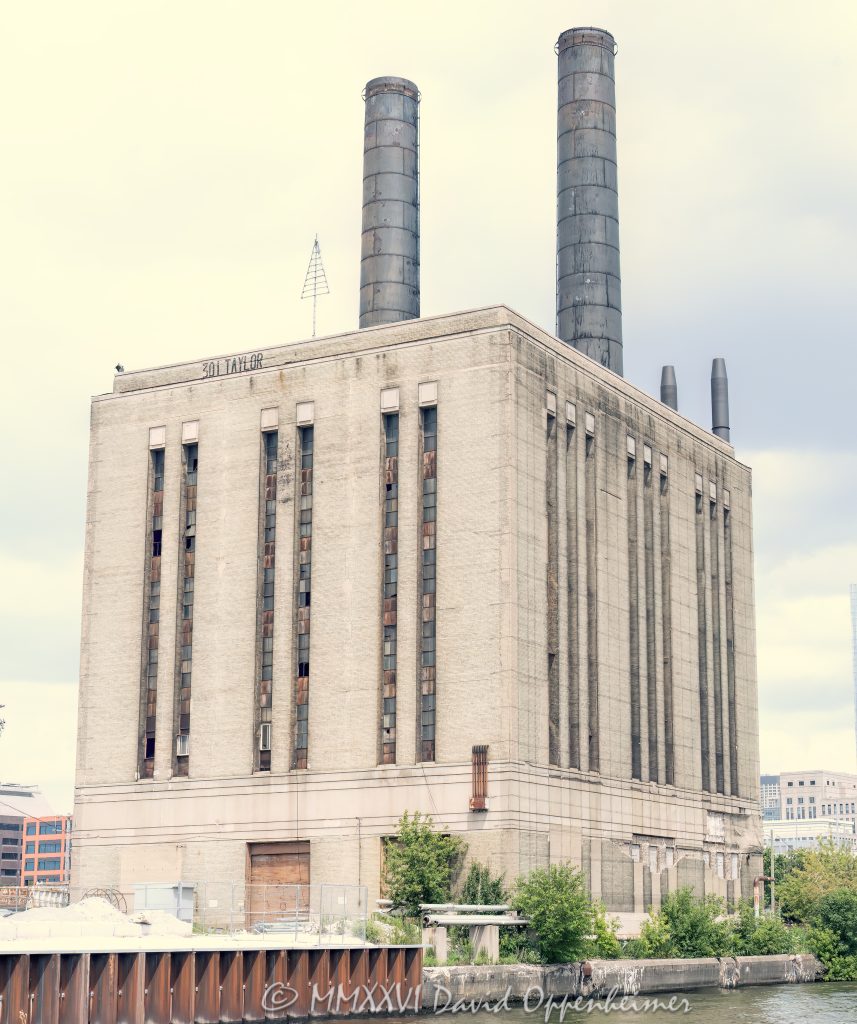 Chicago Union Station Power House at 301 West Taylor Street stands along the South Branch of the Chicago River, showing its Art Moderne industrial facade, massive brick volume, vertical window bands, and twin smokestacks. Designed by Graham, Anderson, Probst & White for the Chicago Union Station Company, the former power and boiler plant supplied steam and electricity for railroad infrastructure and has been the focus of preservation efforts against proposed demolition – © 2026 David Oppenheimer – Performance Impressions photography archives https://performanceimpressions.com Chicago Union Station Power House, Union Station Power House, Union Station Powerhouse, Union Station Boiler Plant, Chicago Union Station Boiler Plant, 301 W Taylor Street, 301 West Taylor Street, 301 W Taylor St, West Taylor Street, Taylor Street, South Loop, South Loop Chicago, downtown Chicago, Chicago Illinois, Chicago IL, 60607, Chicago River, river, South Branch Chicago River, riverfront, waterfront, Chicago riverfront, Chicago waterfront, facade, building exterior, exterior, Art Moderne, Art Deco, Art Moderne facade, Art Deco facade, industrial facade, brick facade, cream brick, brick building, smokestacks, chimneys, twin smokestacks, vertical windows, window bands, industrial building, power house, powerhouse, power plant, boiler plant, steam plant, coal fired plant, utility building, utilities, electricity, steam, electrical power, railroad power, rail infrastructure, train infrastructure, transportation infrastructure, railroad building, railway building, historic building, historic landmark, industrial landmark, endangered building, threatened building, preservation, historic preservation, adaptive reuse, demolition threat, Amtrak, National Railroad Passenger Corporation, Chicago Union Station, Union Station Chicago, Chicago Union Station Company, CUSCo, rail history, railroad history, Chicago railroads, architecture, architectural photography, Chicago architecture, industrial architecture, Art Deco architecture, historic architecture, riverfront architecture, Graham Anderson Probst White, Graham Anderson Probst & White, Daniel Burnham legacy, photorealism, photorealistic, painterly, painterly effect, Illinois architecture, United States, licensing, image licensing, commercial imagery, photography licensing, art, print, fine art, commercial photography, David Oppenheimer, vertical, 1-15156784411